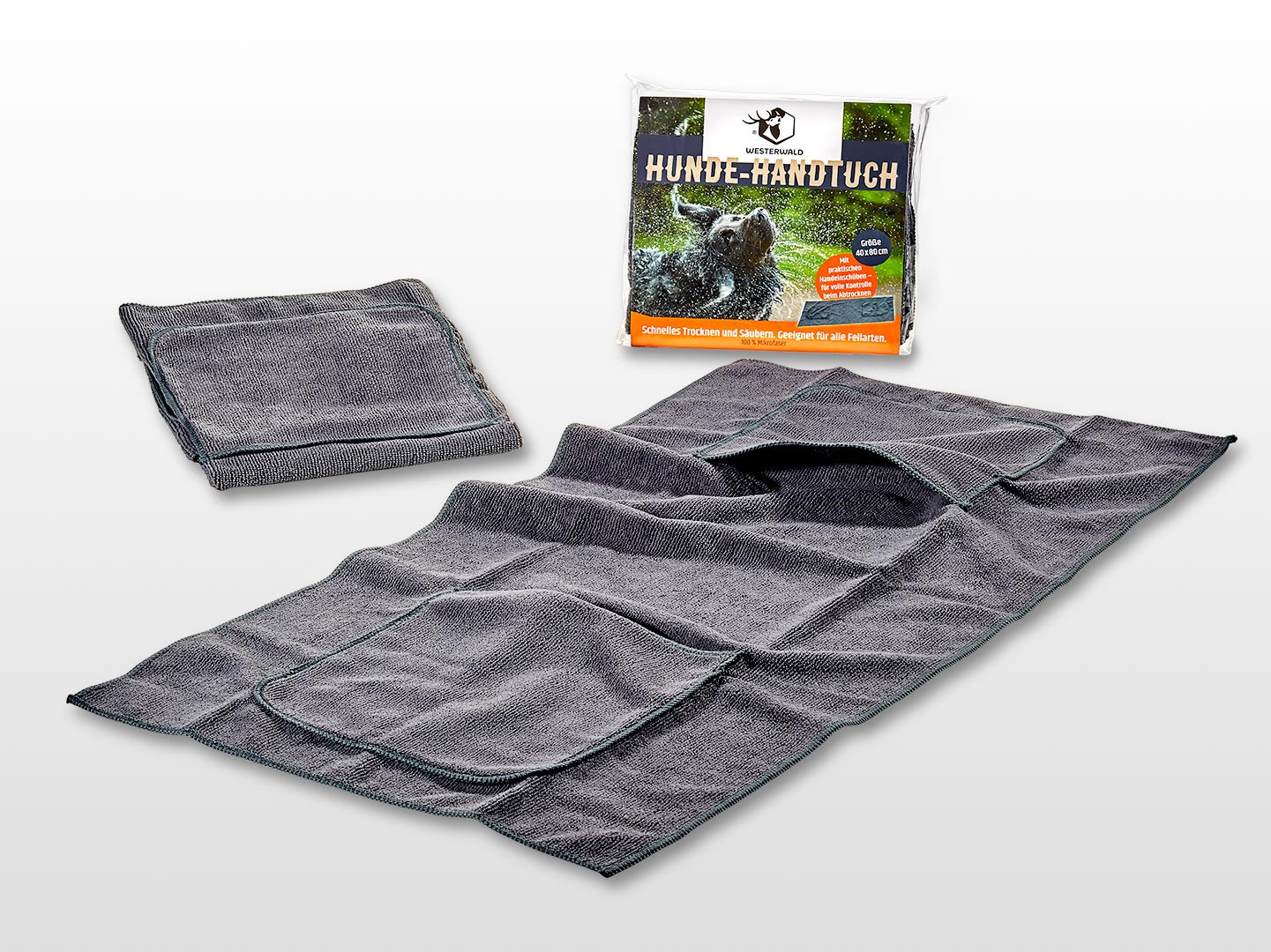 Das graue Hunde-Handtuch von Westerwald Beute (40 x 80 cm) mit praktischen Handeinschüben und umsäumten Rändern wird gefaltet und entfaltet neben der Verpackung gezeigt, die ein nasses Hundebild und den Schriftzug "Hunde-Handtuch" zeigt.