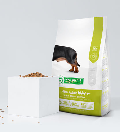 Ein 2-kg-Beutel Nature's Protection NP Geflügel & Garnelen Hundefutter steht aufrecht neben einem weißen Würfel, der mit Kroketten gefüllt ist, mit grünem und gelbem Branding und einem Dackelbild.